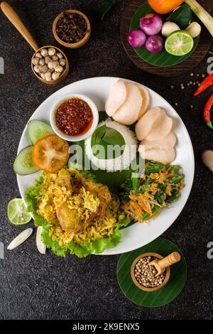 Ayam Goreng Lengkuas oder Gewürze gebratenes Huhn ist ein traditionelles indonesisches gebratenes Huhn mit frischen Kräutern, Gemüse und Chilisauce, serviert in weißen pl Stockfoto