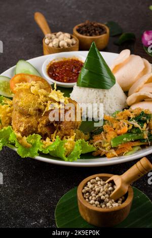 Ayam Goreng Lengkuas oder Gewürze gebratenes Huhn ist ein traditionelles indonesisches gebratenes Huhn mit frischen Kräutern, Gemüse und Chilisauce, serviert in weißen pl Stockfoto