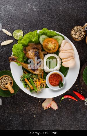 Ayam Bakar oder gebratenes Huhn mit Kräutern und Gewürzen aus Indonesien, serviert auf einem weißen ovalen Teller Stockfoto