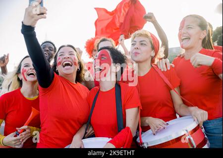 Fröhliche, vielfältige Frauen, die während eines Fußballspiels im Sonnenlicht Selfie machen Stockfoto