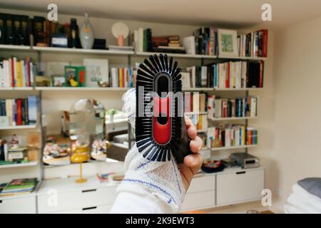 Männliche Hand mit einer bandagierten Hand, die die Vakuumbürste hält - mehrere Regale im Wohnzimmer Stockfoto