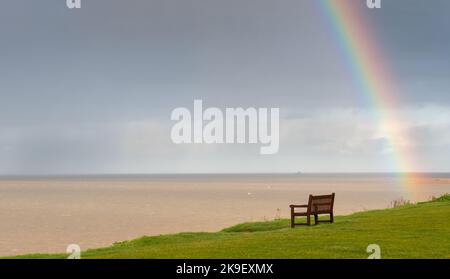 Regenbogen über dem Meer und Holzbank an der Küste zum Entspannen. Atlantischer Ozean england Stockfoto