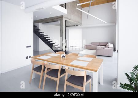 Stilvoller Holztisch in der Küche. Minimalismus.eleganter weißer Kücheninnenraum mit einem großen geräumigen Sofa vor dem Hintergrund einer Treppe Stockfoto