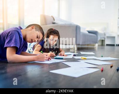 Kreativität überall. Zwei kleine Kinder liegen auf dem Boden und färben sich zu Hause in ihren Malbüchern Bilder ein. Stockfoto