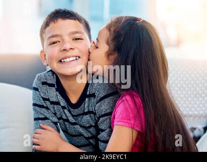 Große Küsse auf der Wange für ihren großen Bruder. Ein entzückendes kleines Mädchen, das ihren großen Bruder auf der Wange zu Hause küsst. Stockfoto