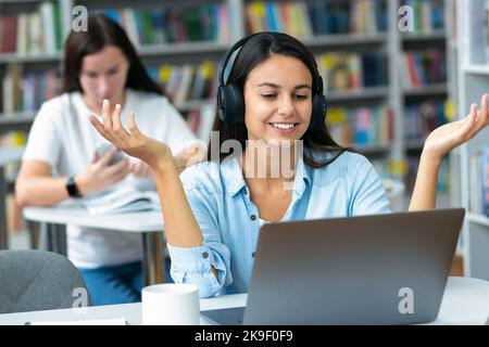 Junge Frau, die in der Verkaufsabteilung mit einem Laptop arbeitet, während sie an ihrem Arbeitsplatz im Büro sitzt und Kunden berät Stockfoto