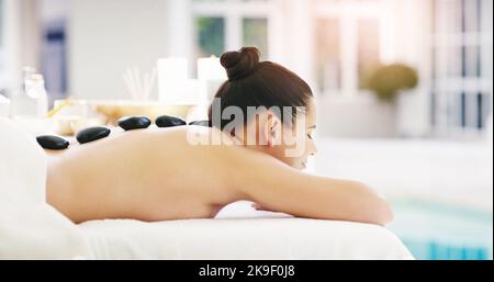 Unsere Behandlungen werden Sie garantiert verjüngen. Eine junge Frau bekommt eine Hot Stone Massage in einem Spa. Stockfoto