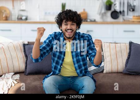 Porträt eines glücklichen Indianers, überglücklich mit guten Nachrichten. Lächelnder Mann mit lockigen Haaren, die eine Geste des „Ja“ zeigen Stockfoto