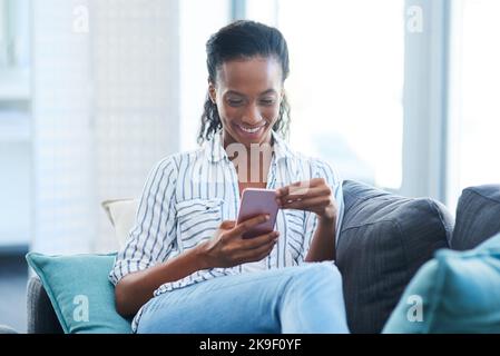 Beim Einchecken mit ein paar ihrer Freunde. Eine junge Frau, die zu Hause auf einem Handy schreibt. Stockfoto