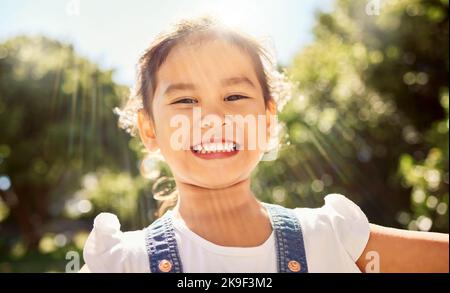 Sommer, Sonnenschein und Porträt des asiatischen Kindes im Park lächeln im Gesicht, spielen und die Natur genießen. Glück, Freude und junge Mädchen, die Spaß im Freien Stockfoto