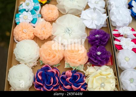 Blumen aus Haargewebe. Haarspangen in verschiedenen Farben. Stoffprodukte für die Dekoration. Rosen aus Stofflappen. Stockfoto