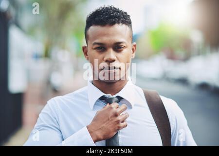 Schauen Sie sich das Teil an, um es zu respektieren. Porträt eines hübschen jungen Geschäftsmannes, der seine Krawatte anpasst, während er in der Stadt unterwegs ist. Stockfoto