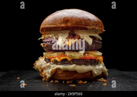 Burger mit zwei Fleischpasteten, Gurken, Tomaten und Käse, auf schwarzem Hintergrund Stockfoto