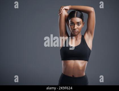 Ich bin meine erste und wichtigste Priorität. Studioportrait einer sportlichen jungen Frau, die ihre Arme vor einem grauen Hintergrund ausstreckt. Stockfoto