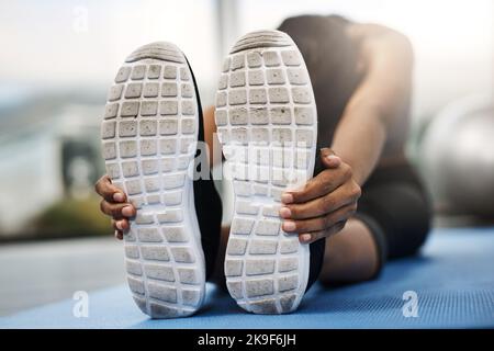 Das einzige schlechte Training ist das, was nicht passiert ist. Eine attraktive junge Frau, die mit dem Kopf nach unten sitzt und Stretching-Übungen auf ihrer Fitnessmatte macht Stockfoto