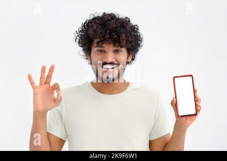 Porträt eines jungen asiatischen Mannes mit Mobiltelefon auf weißem Hintergrund. Männlich mit lockigen Haaren, die ein Smartphone halten Stockfoto