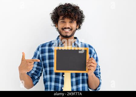 Porträt eines jungen asiatischen Mannes mit Kreidetafel auf weißem Hintergrund. Männchen mit lockigen Haaren, die ein leeres Kreidetafel halten Stockfoto