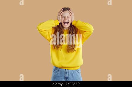 Emotionales Teenager-Mädchen wegen Wut und Groll schreit und weint auf beigem Hintergrund. Stockfoto