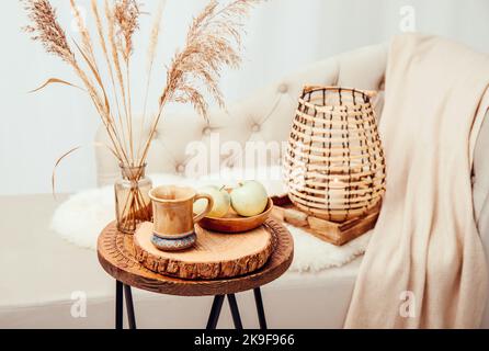 Cozycore oder cottagecore Konzept, warm weich braun beige Interior Design-Objekte. Kuscheliges Wollkaro auf dem Sofa, Kerzenbrenner in Holzlaterne, Teetasse. Stockfoto