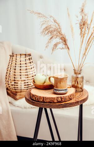 Cozycore oder cottagecore Konzept, warm weich braun beige Interior Design-Objekte. Kuscheliges Wollkaro auf dem Sofa, Kerzenbrenner in Holzlaterne, Teetasse. Stockfoto