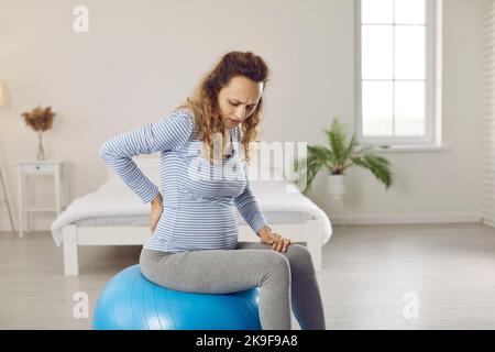 Müde junge, schwanger Frau mit Rückenschmerzen, die an einem ftigen Ball Schmerzlinderung übt Stockfoto