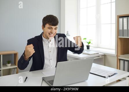 Glücklicher, begeisterter Geschäftsmann, der den Erfolg seines Laptops im Büro feiert Stockfoto