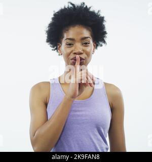 Kannst du ein Geheimnis bewahren? Studioaufnahme einer attraktiven jungen Frau, die mit dem Finger auf den Lippen vor einem grauen Hintergrund posiert. Stockfoto