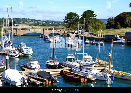 Brücke über den Fluss Axe mit kleinen Fischerbooten und Yachten im Vordergrund und die Landschaft von Devon im Hintergrund, Axmouth, Devon, UK. Stockfoto