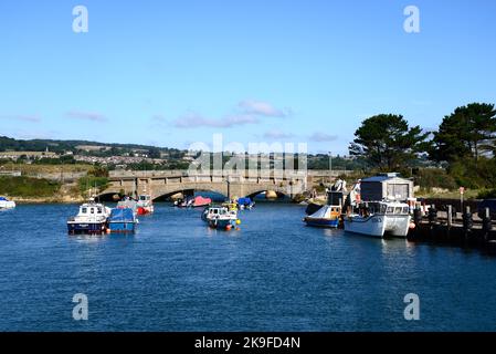 Brücke über den Fluss Axe mit kleinen Fischerbooten im Vordergrund und die Landschaft von Devon im Hintergrund, Axmouth, Devon, Großbritannien. Stockfoto