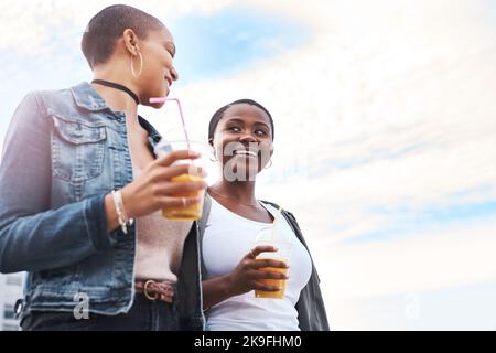Gute Nachrichten bringen ein Lächeln auf jedem Gesicht. Aufnahme zweier junger Frauen, die in der Stadt lachen und dabei ihre kühlen Getränke halten. Stockfoto