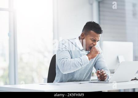 Die langen Tage im Büro werden sich als fruchtbar erweisen. Ein junger Geschäftsmann, der an seinem Schreibtisch sitzt, gähnt und ermüdend aussieht. Stockfoto