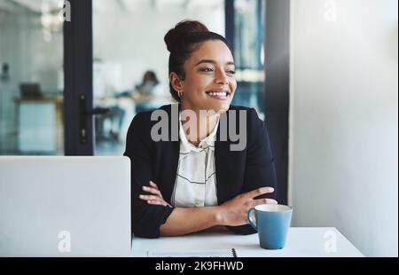 Nächstes Karriereziel, hier komme ich. Eine selbstbewusste junge Geschäftsfrau, die an ihrem Schreibtisch in einem modernen Büro arbeitet. Stockfoto