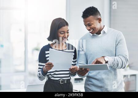 Teamwork macht den Traum klar: Zwei junge Geschäftsleute stehen in ihrem Büro und arbeiten mit einem digitalen Tablet zusammen. Stockfoto