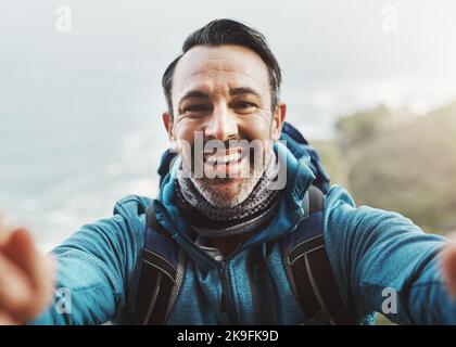 Glücklich zu sein geht nie aus dem Stil. Porträt eines Mannes mittleren Alters, der ein Selfie in den Bergen gemacht hat. Stockfoto