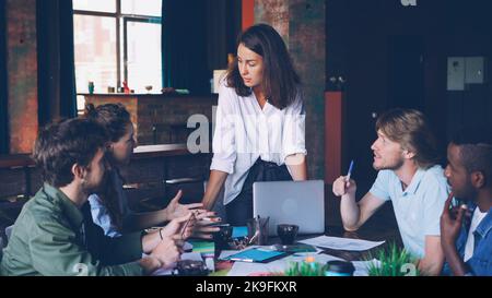 Ein kreatives Team aus jungen Fachleuten entwickelt während eines Geschäftstreffens im Büro eine Arbeitsstrategie. Männer und Frauen sitzen am Tisch, gestikulieren und reden. Stockfoto