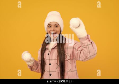 Staunende Kind in Hut und Fäustlinge spielen Schneebälle auf gelbem Hintergrund, Kindheit Stockfoto