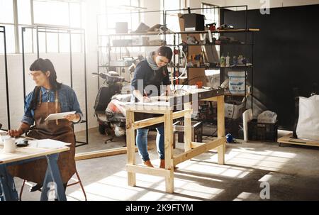 Hier schaffen sie. Zwei attraktive junge kreative Kunsthandwerkerinnen, die in ihrer Werkstatt arbeiten. Stockfoto