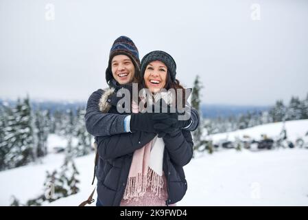 Die beste Zeit zum Kuscheln ist im Winter. Ein glückliches junges Paar genießt sich beim draußen im Schnee. Stockfoto