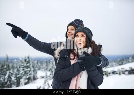 Alles ist magisch, wenn es schneit. Ein glückliches junges Paar genießt sich, während sie draußen im Schnee. Stockfoto