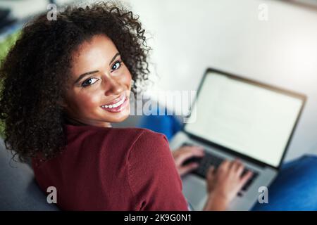 Bleiben Sie mit Dingen in Verbindung, die Sie glücklich machen. Porträt einer jungen Frau, die einen Laptop benutzt, während sie sich zu Hause auf dem Sofa entspannt. Stockfoto