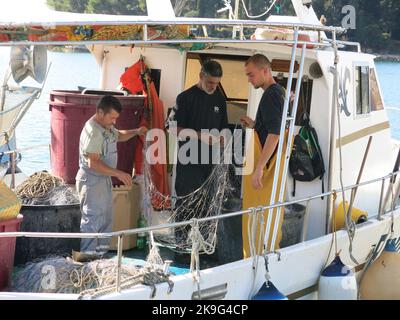Im kroatischen Hafen Rovinj auf der Halbinsel Istrien entwirren drei Fischer ihre Netze an Bord ihres Fischerbootes. Stockfoto