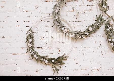 Weihnachten, Neujahrskomposition. Festliche Kranze mit weißen Kugeln aus Weihnachtsbaum, Tannenzweige auf weißer Ziegelwand. Gemütliche skandinavische Einrichtung. Frohe Feiertage, Vorlage. Grußkarte. 2023. Stockfoto