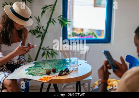 Ein schwarzer Mann und ein kaukasisches Weibchen ruhen in einer Kaffeebar. Sie chatten auf ihren Telefonen Stockfoto