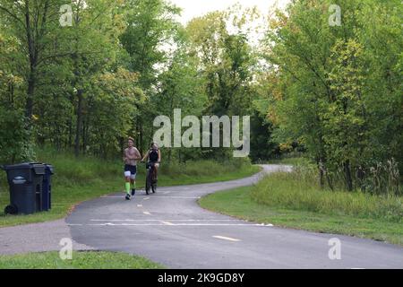 Ein Mann, der läuft, und eine Frau, die auf einem Waldweg radelt Stockfoto