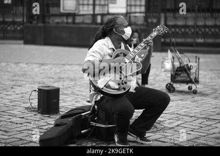 Ein schwarzer Straßenmusiker in einer Maske, der im Dorf in New York Gitarre spielt Stockfoto