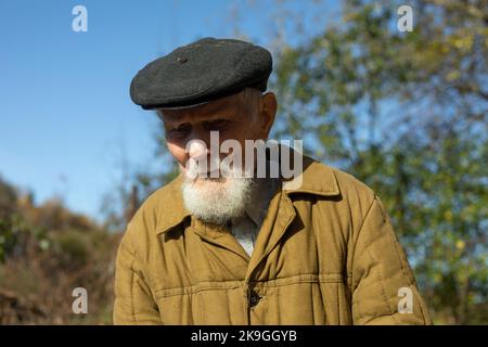 Alter Mann mit grauem Bart und Mütze. Mann von 92 Jahren. Alter Mann im Garten. Russischer Großvater in schwarzer Mütze. Stockfoto