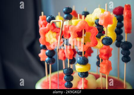 Buntes Fruchtdessert zum Geburtstag eines Kindes. Auf Zahnstocher werden verschiedene Fruchtformen gesetzt. Wassermelone, Ananas, Melone und Heidelbeeren. Stockfoto