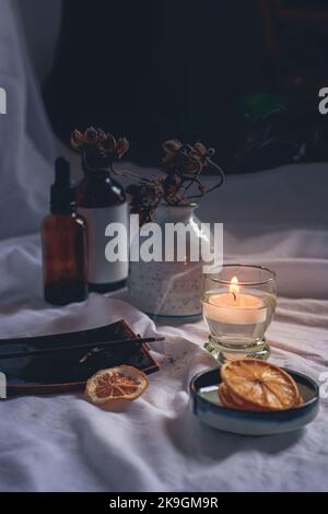 Vertikale Aufnahme von Flaschen mit ätherischem Öl, getrockneten Zitronenscheiben und einer Teekerze für ein gemütliches Ambiente im Herbst Stockfoto