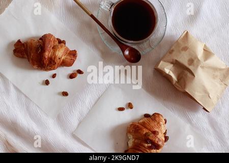 Blick von oben auf eine Tasse schwarzen Kaffee und ein Croissant für ein einfaches und entspannendes französisches Frühstück Stockfoto