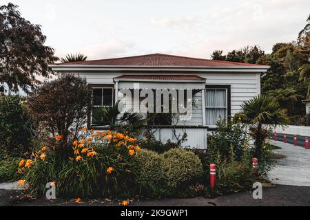 Hübsches Holzhaus in einer engen Straße, umgeben von orangefarbenen Blumen und grünen Pflanzen, in einem ruhigen und ruhigen Dorf unter einem bewölkten Himmel, westlich Stockfoto